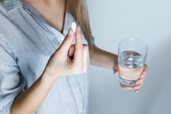 picture of a person with a pill and a glass of water in her hands