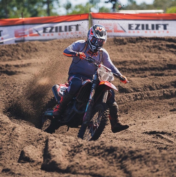 A motocross rider taking a sharp turn on a dirt track, kicking up sand as they lean into the curve. The bike is equipped with a sturdy and stylish bike seat cover.