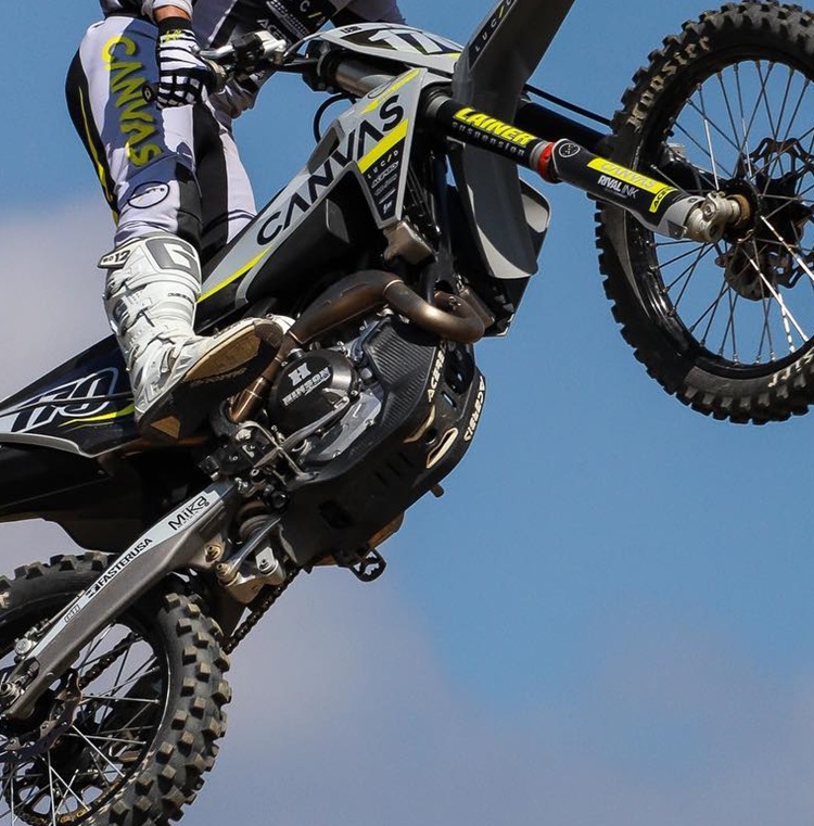 A motocross rider performing a high jump, with a clear view of the bike's underside showing the skid plate