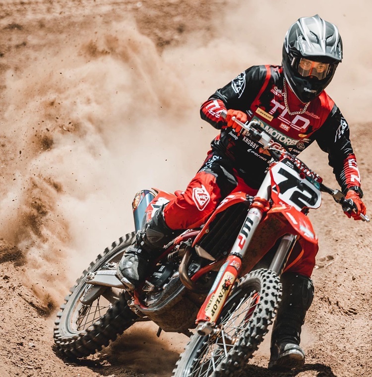 A motocross rider speeding through a dirt track, leaving a cloud of dust behind. The bike features a high-quality bike seat cover designed for extreme sports.